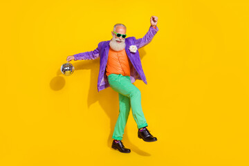 Fototapeta na wymiar Full length photo of pretty attractive guy dressed violet velvet jacket holding disco ball dancing isolated yellow color background