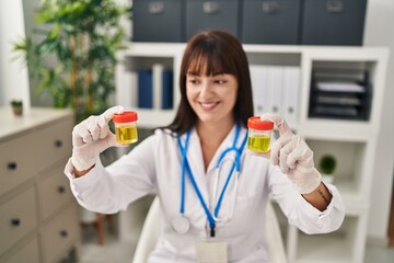 Young beautiful hispanic woman doctor comparing urine test tubes at clinic