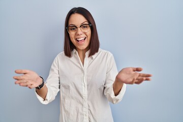 Young hispanic woman standing over white background smiling cheerful offering hands giving...