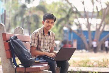 Portrait of Indian boy using laptop while attending the online classes in park	
