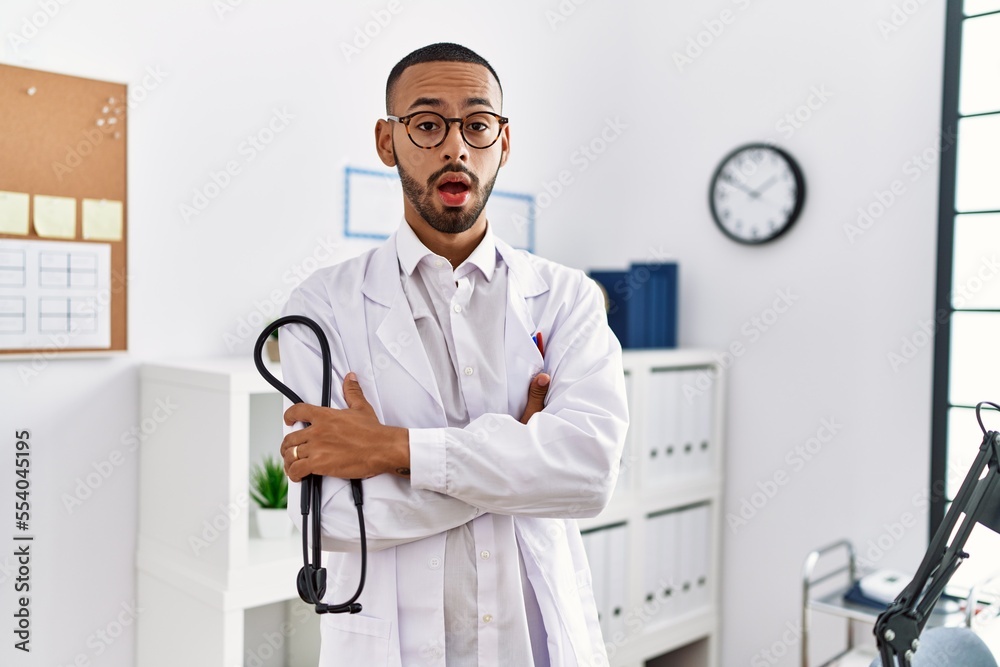 Sticker African american doctor man holding stethoscope at the clinic clueless and confused expression. doubt concept.