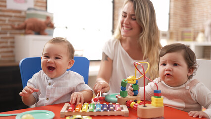 Obraz na płótnie Canvas Teacher and preschool students playing with toys sitting on table at kindergarten
