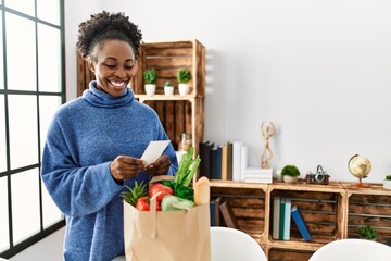 African american woman smiling confident reading food receipt at home