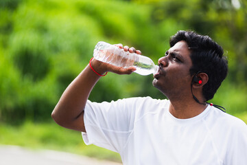 Close up Asian young sport runner black man wear athlete headphones he drinking water from a bottle after running at the outdoor street health park, healthy exercise workout concept