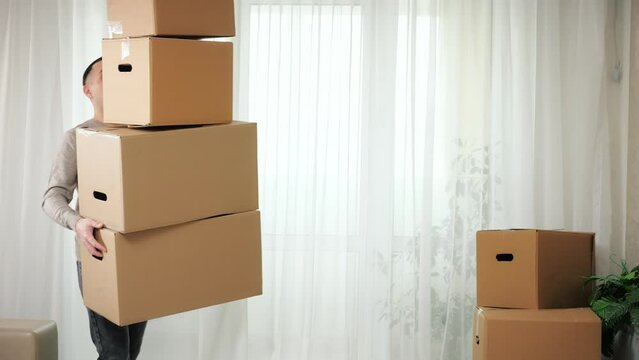 Man carries stack of boxes in arms and falls down on floor in new apartment. Black-haired guy helps with moving into new house and tries to hold boxes, closeup