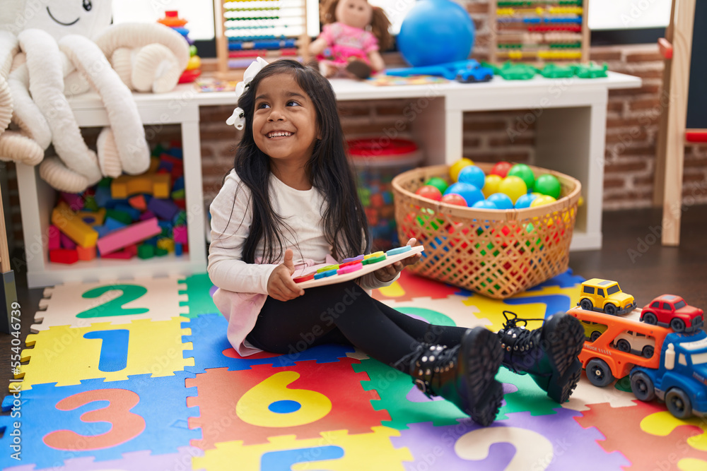 Sticker Adorable hispanic girl playing with maths puzzle game sitting on floor at kindergarten