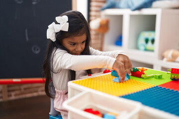 Fototapeta na wymiar Adorable hispanic girl playing with construction blocks sitting on table at kindergarten