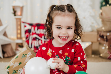 happy little girl at home holding baubles during christmas time