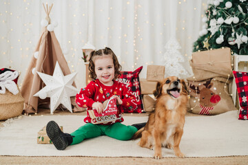 cute little girl at home standing with dog during christmas time