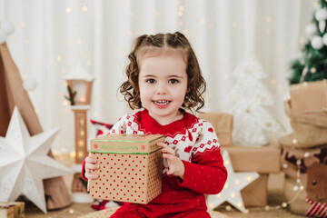 smiling cute little girl at home during christmas time holding gift box