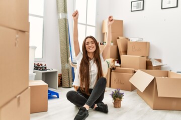 Young hispanic woman smiling confident sitting on floor with dog at new home