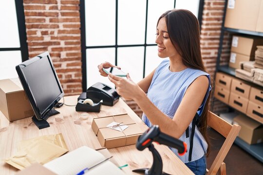 Young beautiful hispanic woman ecommerce business worker make photo to package by smartphone at office