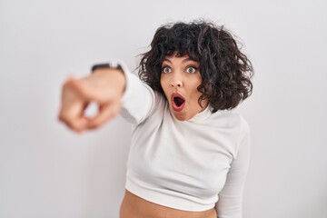 Fototapeta na wymiar Hispanic woman with curly hair standing over isolated background pointing with finger surprised ahead, open mouth amazed expression, something on the front