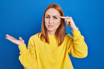 Young woman standing over blue background confused and annoyed with open palm showing copy space...