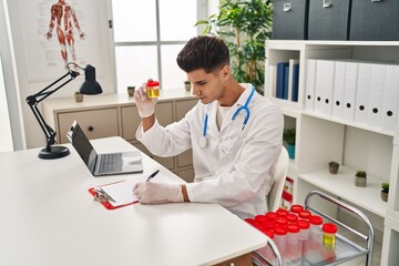 Young hispanic man wearing doctor uniform analysing urine test tube at clinic