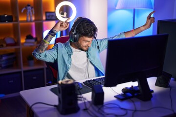 Young hispanic man streamer playing video game with winner expression at gaming room