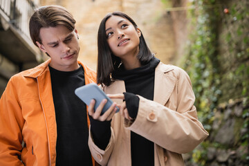 Low angle view of asian woman pointing at smartphone near boyfriend outdoors.