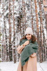 A smiling girl with a green scarf in a coat stands in the snow in winter