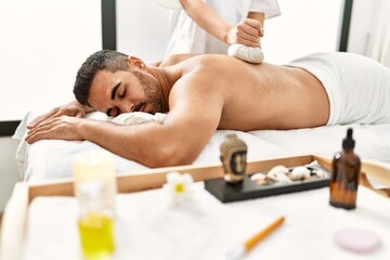 Obraz na płótnie Canvas Young hispanic man having back massage using thai bags at beauty center