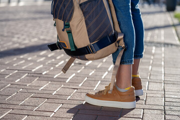 Woman legs in jeans and brown sneakers shoes with backpack