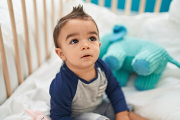 Adorable hispanic toddler sitting on cradle with relaxed expression at bedroom