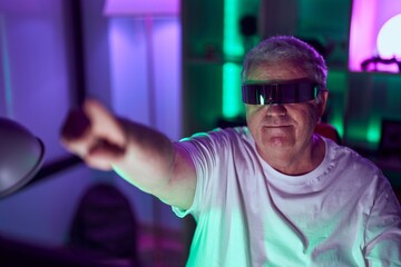 Middle age grey-haired man streamer playing video game using virtual reality glasses at gaming room