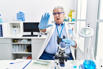 Senior caucasian man working at scientist laboratory doing stop gesture with hands palms, angry and frustration expression