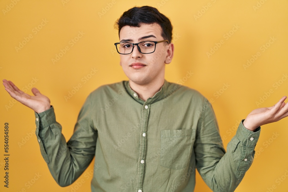 Poster Non binary person standing over yellow background clueless and confused expression with arms and hands raised. doubt concept.