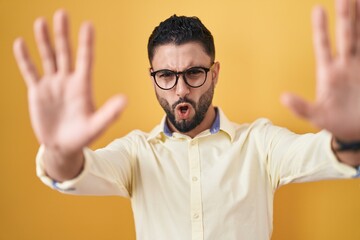 Fototapeta premium Hispanic young man wearing business clothes and glasses doing stop gesture with hands palms, angry and frustration expression