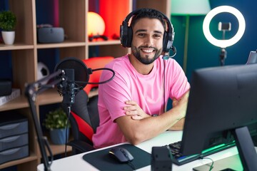 Young arab man streamer smiling confident sitting with arms crossed gesture at gaming room