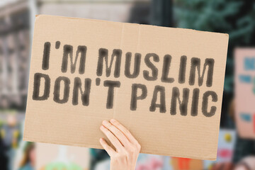 The phrase " Iâ€™m Muslim donâ€™t panic " on a banner in men's hand with blurred background. Hate. Equality. Human rights. Protest. Anti Muslim. Anti-muslim. Multiracial. Racism