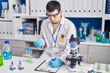 Young man scientist writing on document measuring liquid at laboratory