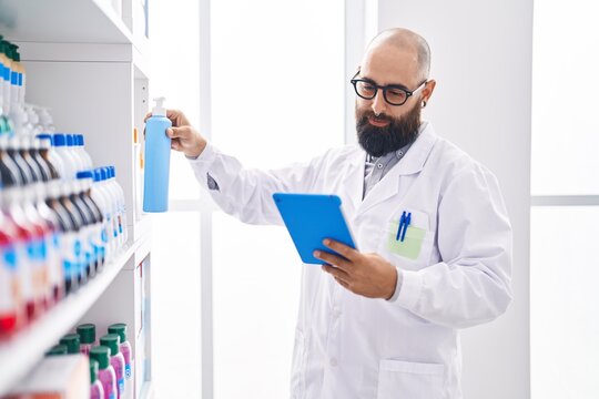 Young bald man pharmacist using touchpad holding cream bottle at pharmacy