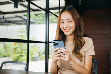 Beautiful Asian female hands holding and typing to communicate with others through on mobile phone, young woman using smartphone for shopping online at cafe coffee shop near windows in morning