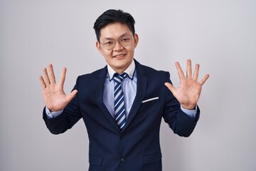 Young asian man wearing business suit and tie showing and pointing up with fingers number ten while smiling confident and happy.