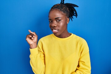 Beautiful black woman standing over blue background pointing aside worried and nervous with...