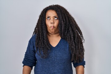 Plus size hispanic woman standing over white background making fish face with lips, crazy and comical gesture. funny expression.