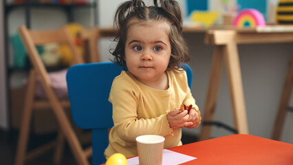 Adorable hispanic girl student sitting on table drawing on paper at kindergarten