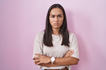 Young hispanic woman standing over pink background skeptic and nervous, disapproving expression on face with crossed arms. negative person.