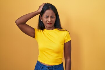 Young indian woman standing over yellow background confuse and wondering about question. uncertain...