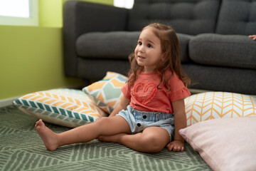 Adorable hispanic girl sitting on floor with relaxed expression at home