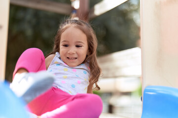 Fototapeta na wymiar Adorable hispanic girl sitting on slide playing at park playground