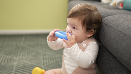 Adorable toddler bitting plastic hoop sitting on floor at home