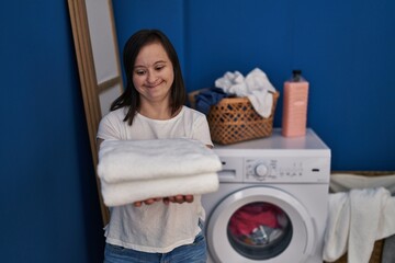 Down syndrome woman smiling confident holding clean towels at laundry room