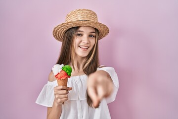 Teenager girl holding ice cream pointing to you and the camera with fingers, smiling positive and...