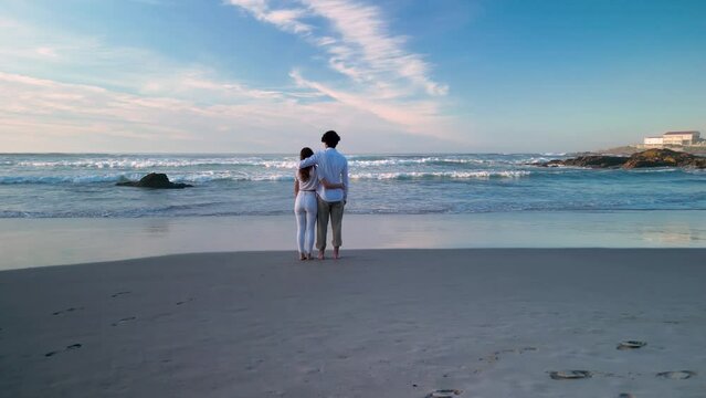 Sweet Couple Looks At The Waves In Caion Paradise Beach In Spain. Aerial Drone Shot