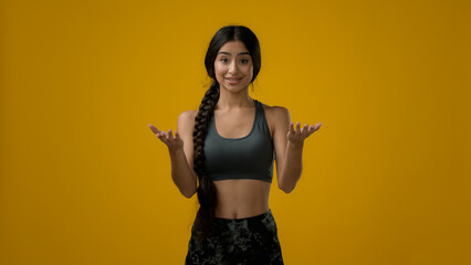 Ethnic woman Indian sporty girl sports trainer lady sport athlete female in yellow studio talk looking to camera explain exercise showing hand arm and neck head stretching pose stretch workout online