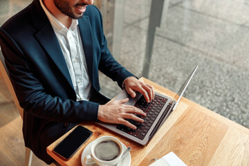Close up of unrecognizable businessman working on laptop in coffee shop working space