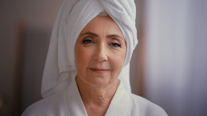 Caucasian old senior mature attractive middle-aged woman 60s lady 50s female model wearing bathrobe and white towel on head with wrinkled face looking at camera. Advertising skin care spa procedures