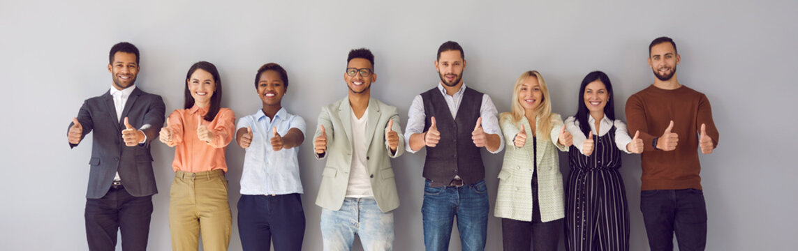 Studio team portrait of many happy international multicultural multiracial multiethnic males and females with optimistic approving attitude standing in row showing thumbs up together Banner background
